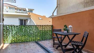Un patio con tavolo e sedie, una recinzione verde e un edificio con tetto in tegole sullo sfondo.