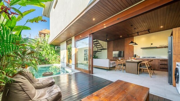 A modern house with a wooden deck, a pool, a dining area, and a kitchen. - Nala Villa Bali (Badung)