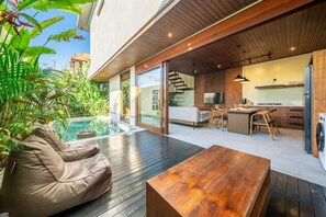 A modern house with a wooden deck, a pool, a dining area, and a kitchen. - Nala Villa Bali (Badung)