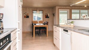Moderni keittiö, jossa on puiset kaapit, ruokapöytä ja sisäänrakennettu astianpesukone.