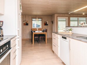 A modern kitchen with wooden cabinets, a dining table, and a built-in dishwasher. - 6 Person Holiday Home in Herning (Herning)
