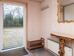 A room with a wooden door leading to a gravel area, a small wooden shelf, a white radiator, and a gold-framed mirror. - 6 Person Holiday Home in Herning (Herning)