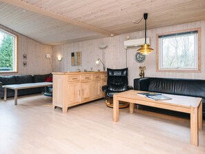 A wooden-paneled room with a sofa, a dining table, a cabinet, and a black leather chair. - 6 Person Holiday Home in Herning (Herning)