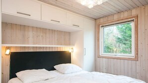 Makuuhuone, jossa on sänky, puuseinät, ikkuna, josta on näkymä puita kohti, ja sisäänrakennetut kaapit.