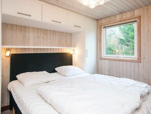 A bedroom with a bed, wooden walls, a window with a view of trees, and built-in cabinets. - 6 Person Holiday Home in Herning (Herning)