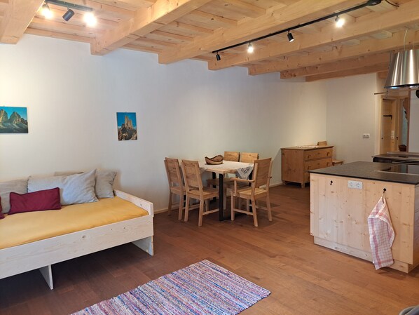 Une pièce chaleureuse comprenant un lit, une table à manger avec des chaises, un coin cuisine et des poutres apparentes en bois au plafond.