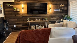 Ein modernes Wohnzimmer mit einem an einer Holzwand montierten Flachbildfernseher, einem weißen Sofa und einem Couchtisch mit dekorativen Accessoires.