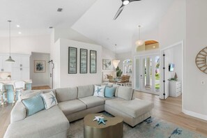 A modern living room with a sectional sofa, a round coffee table, and a dining area with chairs. - Bella Vista - 3BBR/3BA Coastal Retreat with Heated Pool & Spa (Marco Island)