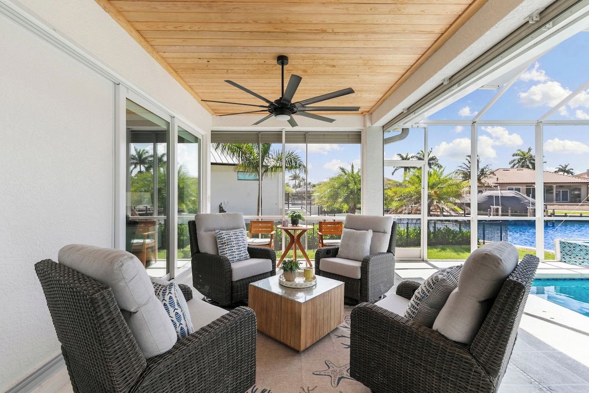 A covered outdoor seating area with wicker furniture, a ceiling fan, and a view of a swimming pool.