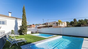 Une piscine divisée en deux zones distinctes, entourée d’un mur blanc et d’un espace verdoyant agrémenté de chaises longues.