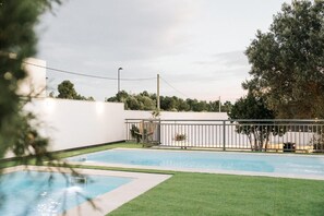 Ein Swimmingpool mit einer umlaufenden Rasenfläche, einer weißen Wand und einem Baum.