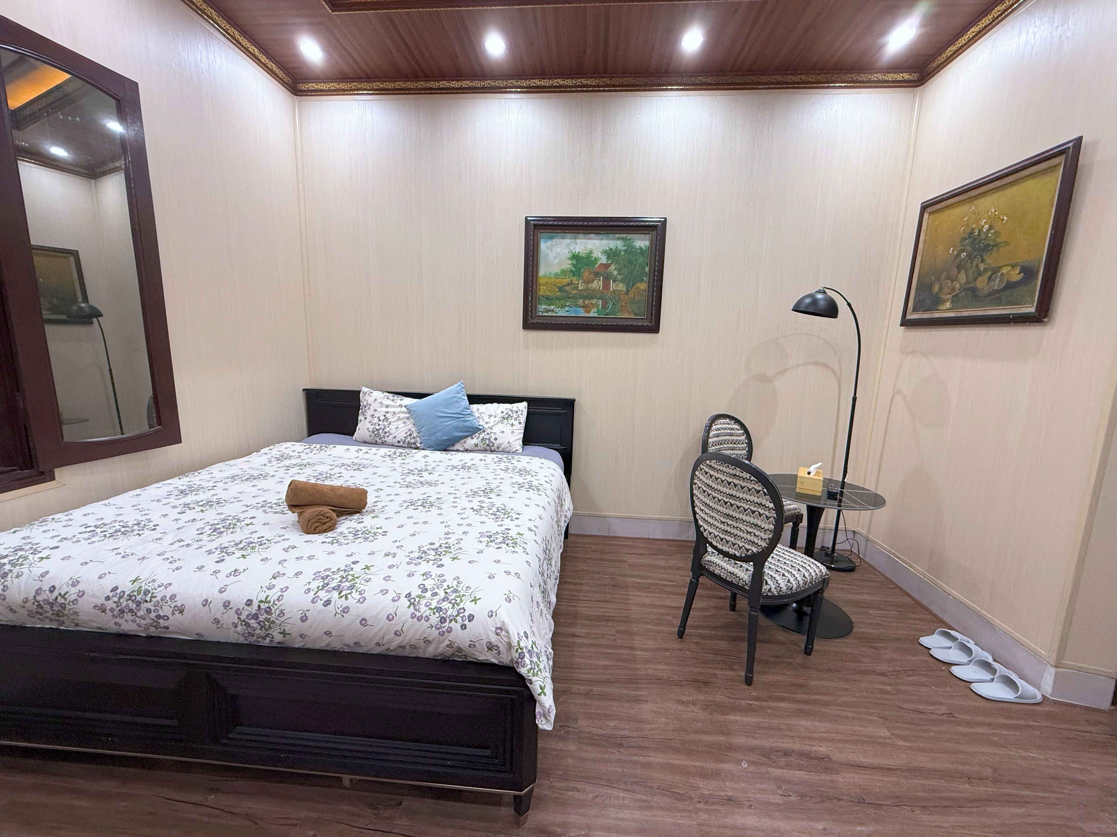 A bedroom with a bed, a desk, a chair, a lamp, and a painting on the wall.
