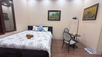 A bedroom with a bed, a desk, a chair, a lamp, and a painting on the wall.