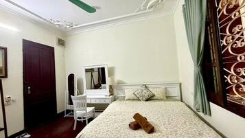 A bedroom with a bed, a desk, a chair, a ceiling fan, and a window with curtains.