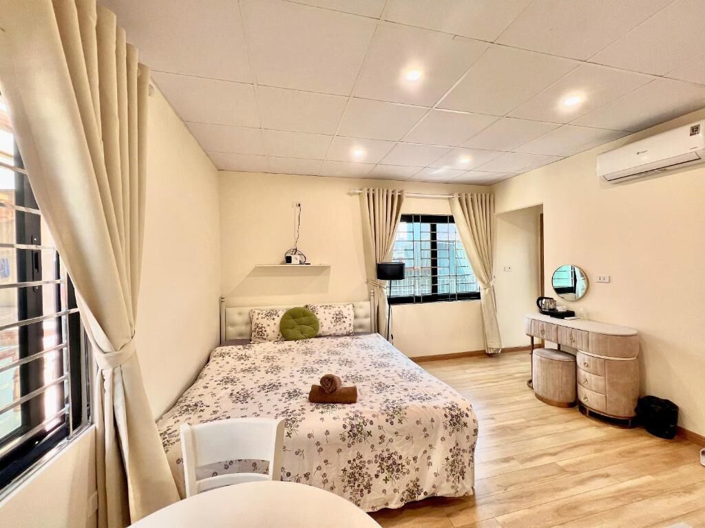 A bedroom with a bed, a bedside table, a chair, a mirror, and a window with curtains.