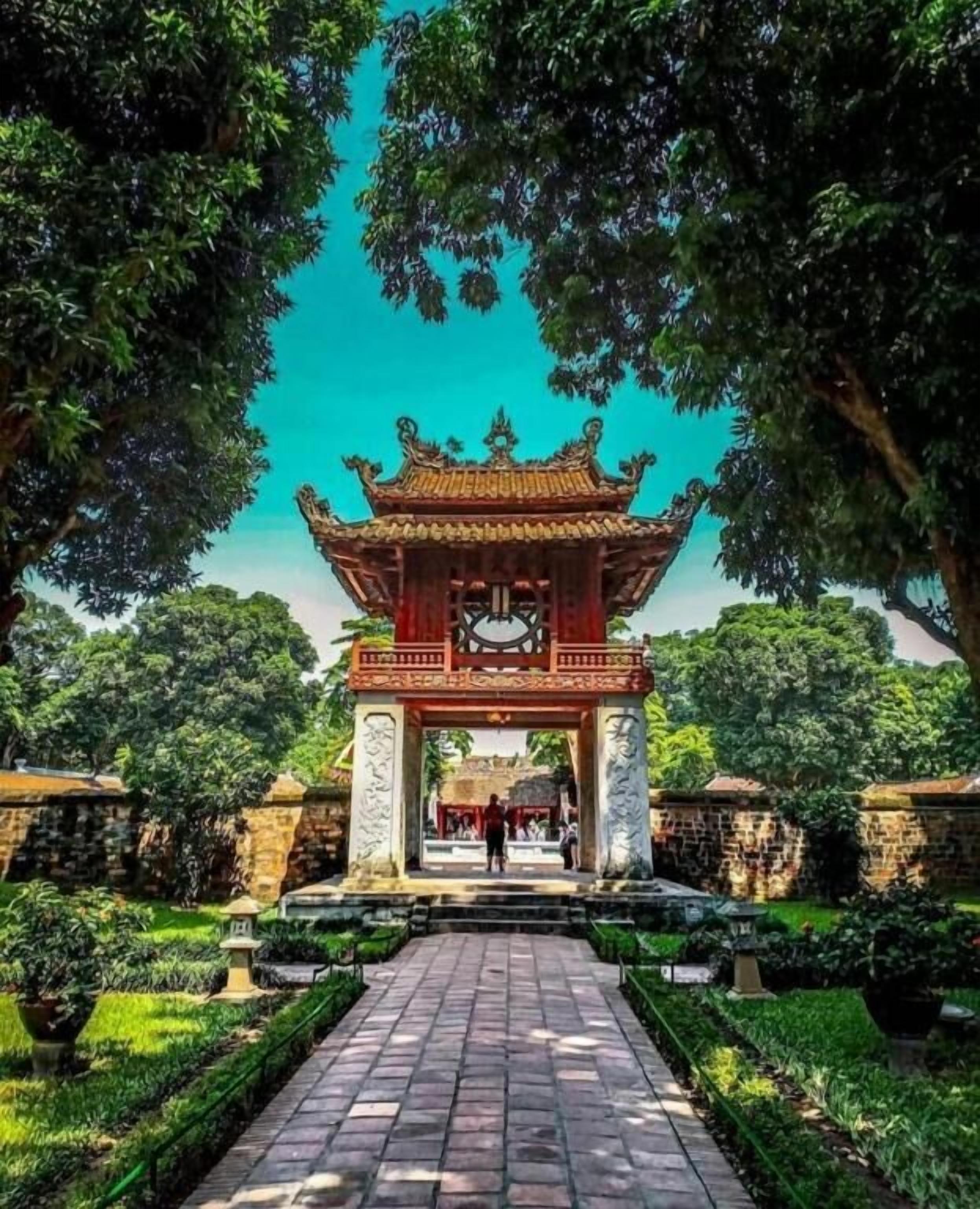 A traditional gate with intricate carvings, a paved pathway, and well-maintained greenery.