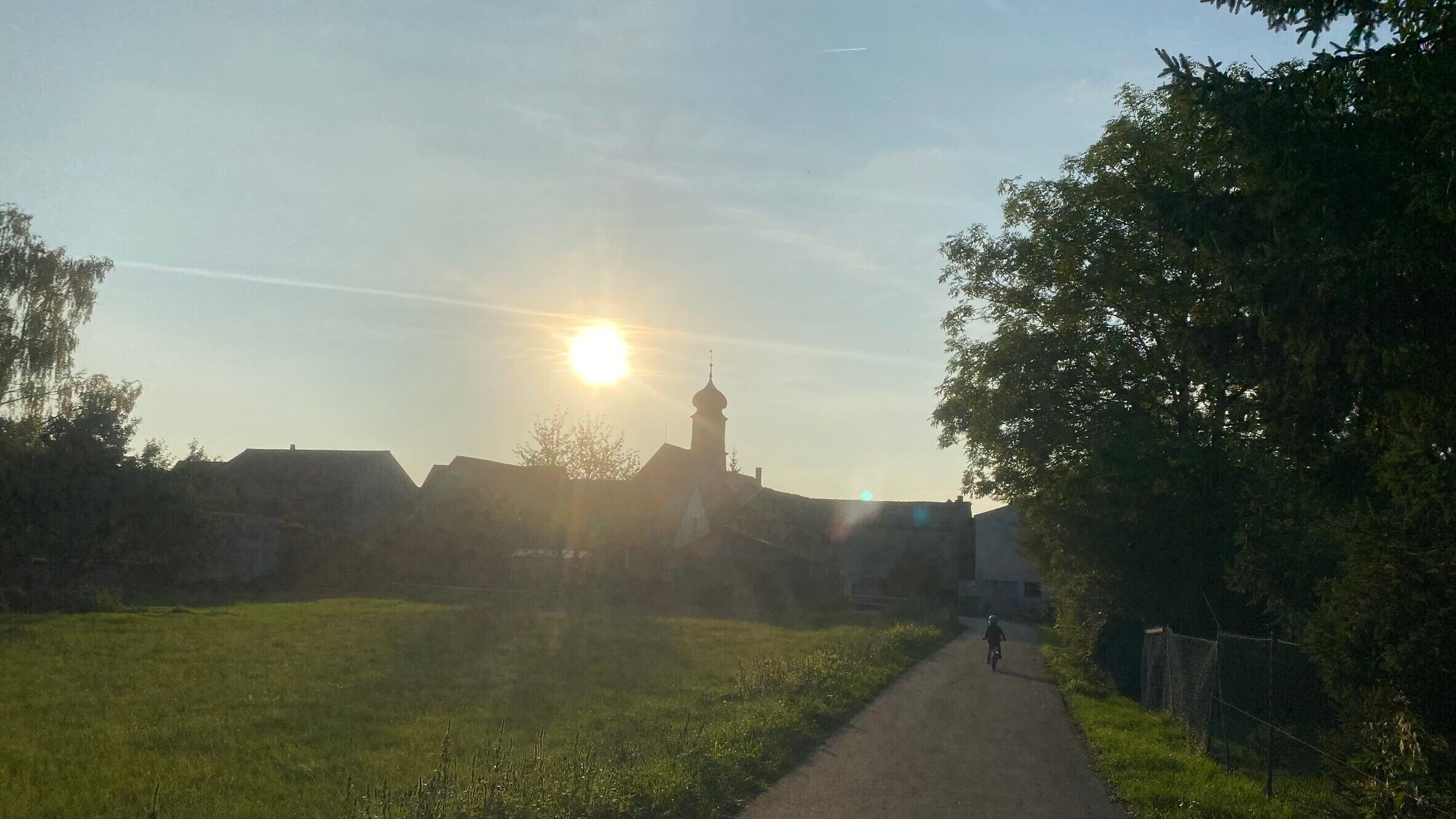 En lantlig stig som leder till en kyrka med ett framträdande torn, omgiven av grönska och en klar himmel.