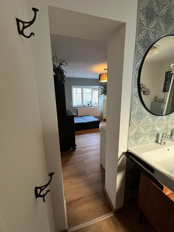 A hallway leading to a bedroom with a window, a bedside table, and a mirror.