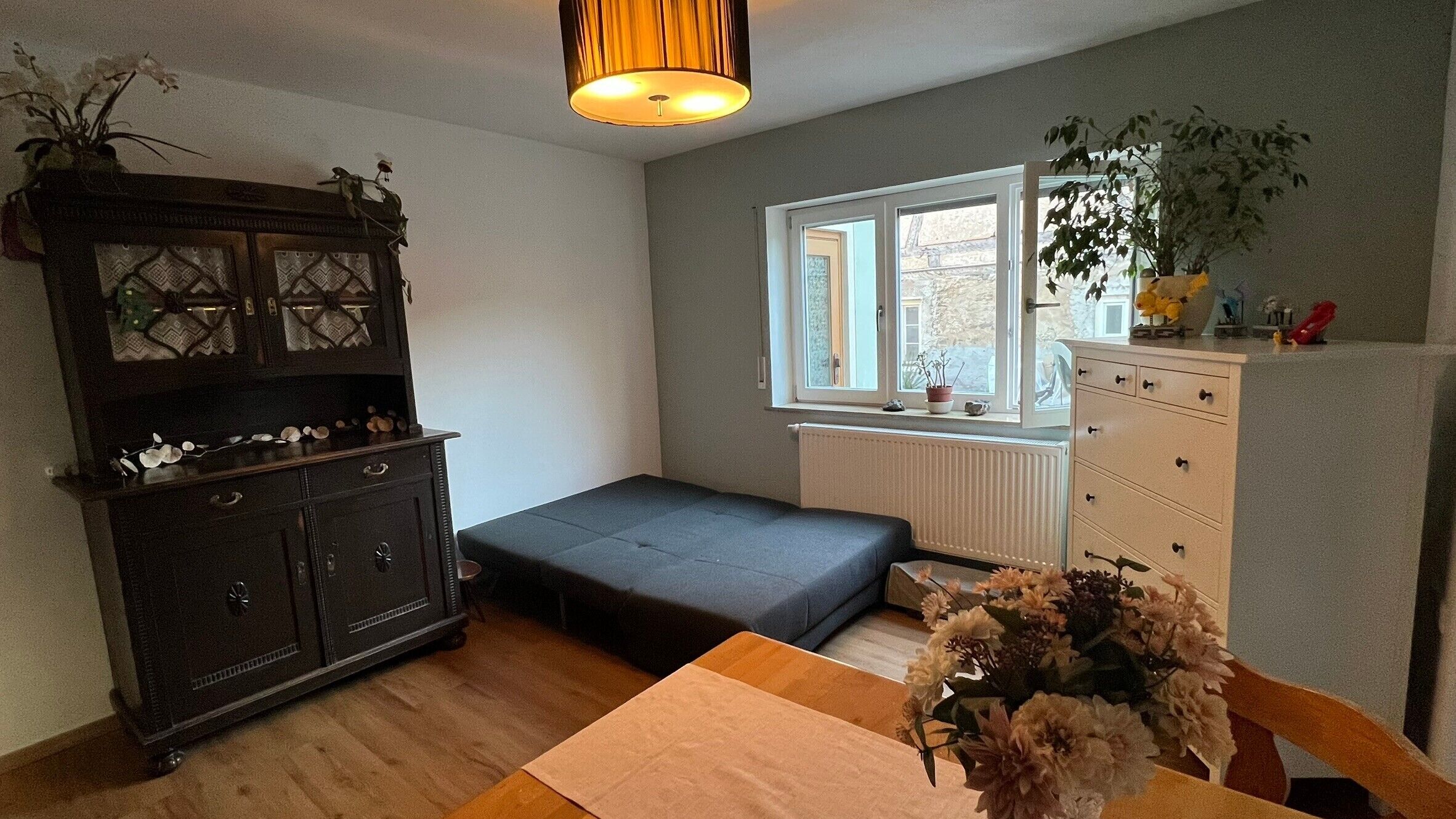 Une pièce avec un lit, une commode, une fenêtre et une plante.