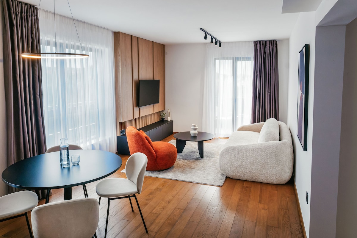 A modern living room with a round dining table, a sofa, and a flat-screen TV mounted on the wall.