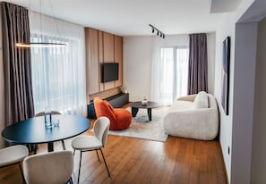 Una sala de estar moderna con una mesa de comedor redonda, un sofá y un televisor de pantalla plana montado en la pared.