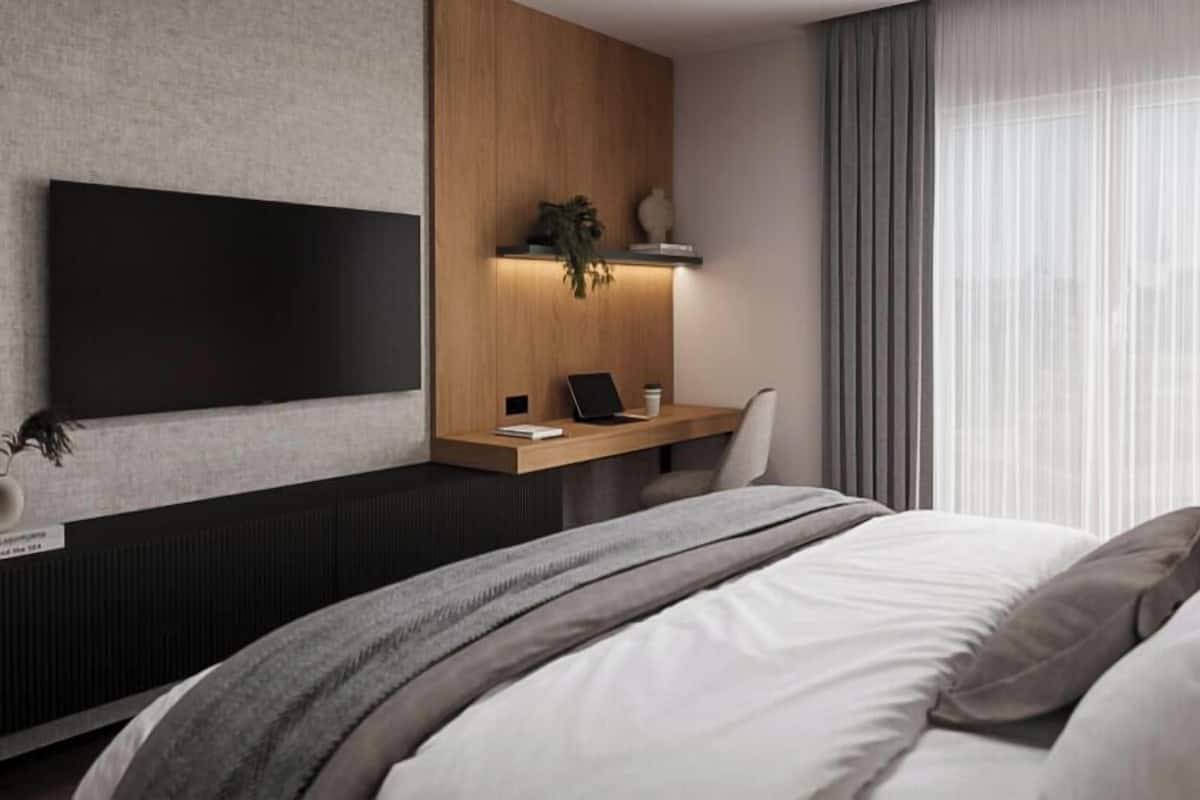 Moderni hotellihuone, jossa on suuri sänky, työpöytä kannettavalla tietokoneella, taulutelevisio ja ikkuna, jossa on verhot.
