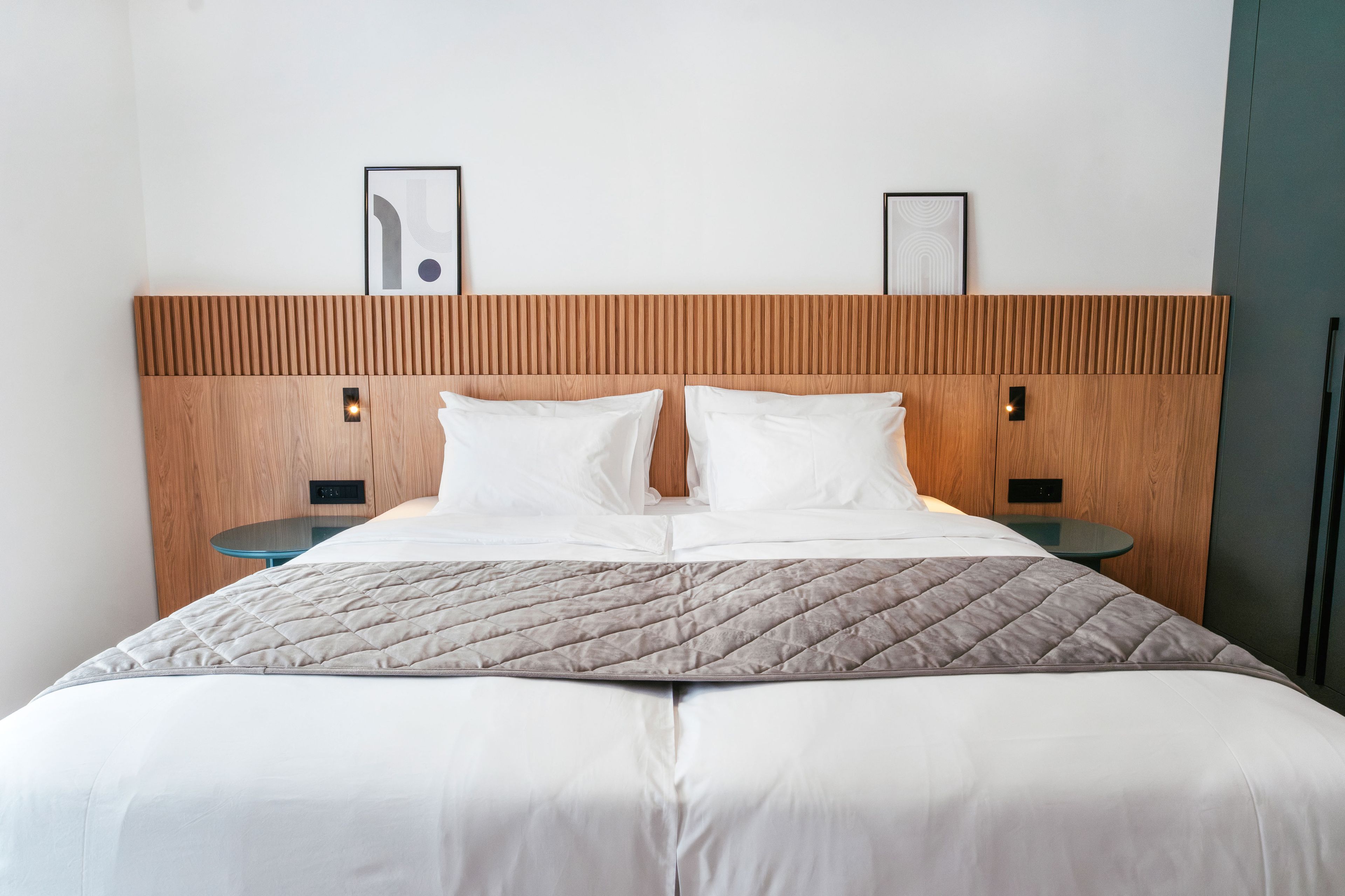 Une chambre d’hôtel avec une tête de lit en bois, deux tables de chevet et un lit avec une literie blanche.