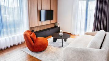 Una sala moderna con un televisor de pantalla plana montado en una pared de madera, un sillón rojo, un sofá blanco y una pequeña mesa redonda.