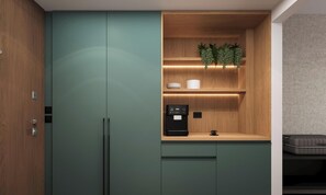 Una kitchenette compacta con cafetera integrada, una pequeña estantería con plantas decorativas y una encimera de madera.