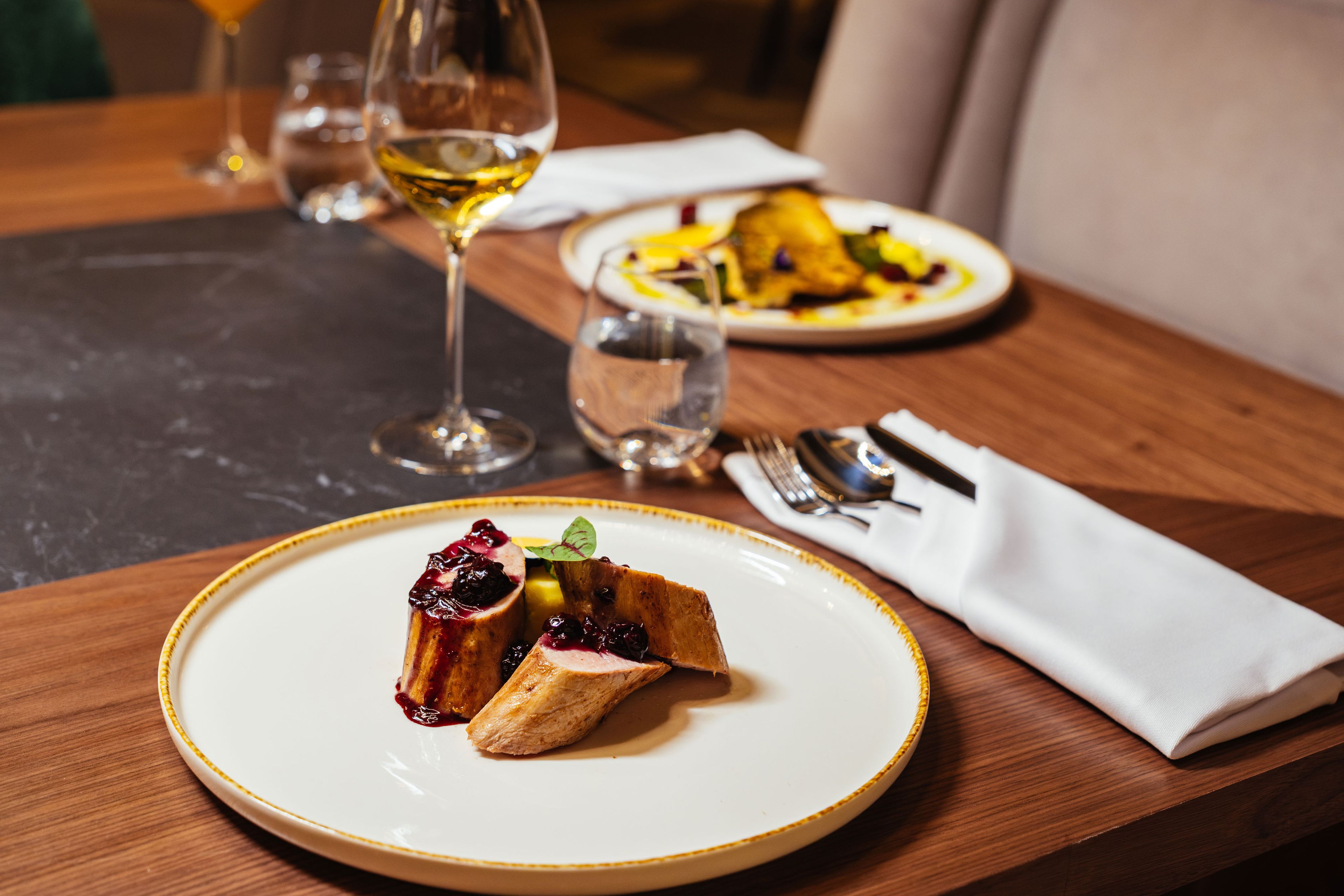 A dining table with a plate of food, a glass of wine, and cutlery.
