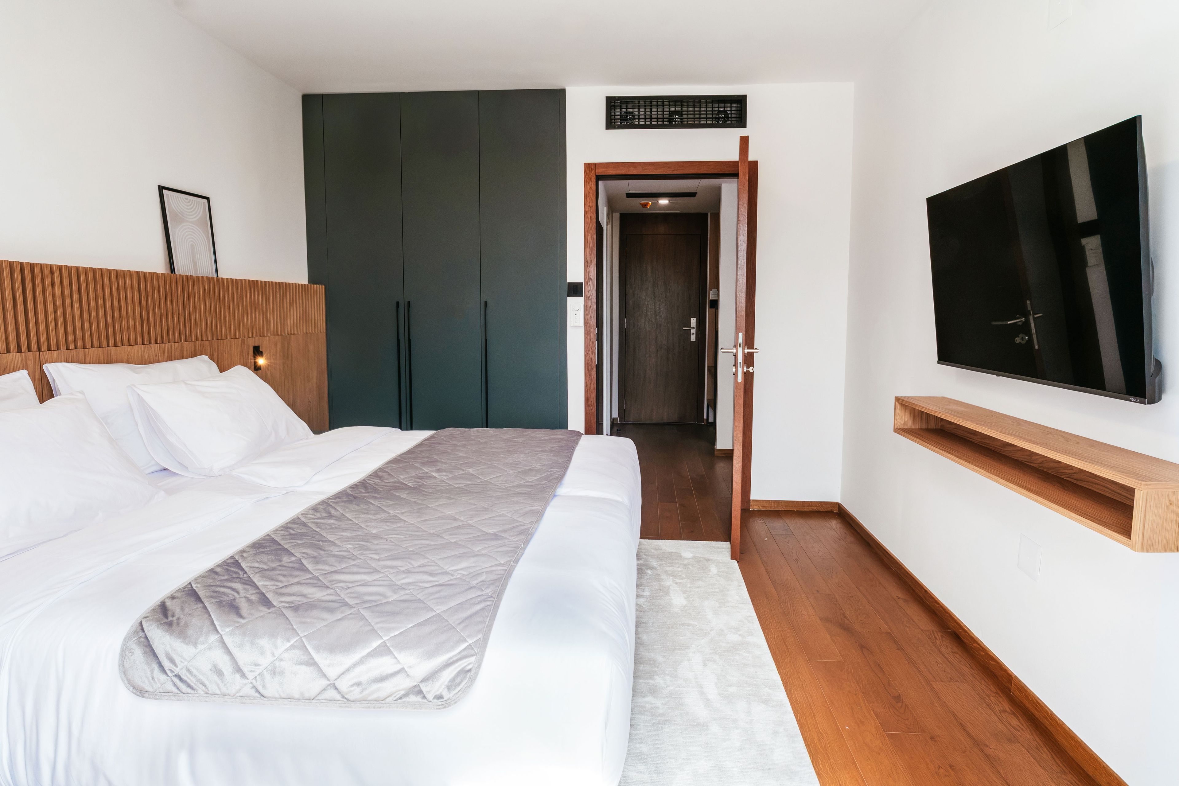 Ein modernes Schlafzimmer mit einem großen Bett, einem an der Wand befestigten Fernseher und einem Kleiderschrank.