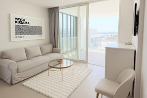 Ein modernes Wohnzimmer mit einer Couch, einem Couchtisch, einem Sessel, einem großen Fenster mit Ausblick und einem gerahmten Kunstwerk an der Wand.