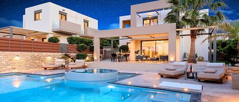 A modern outdoor pool area with a clear night sky, a stone wall, and lounge chairs.