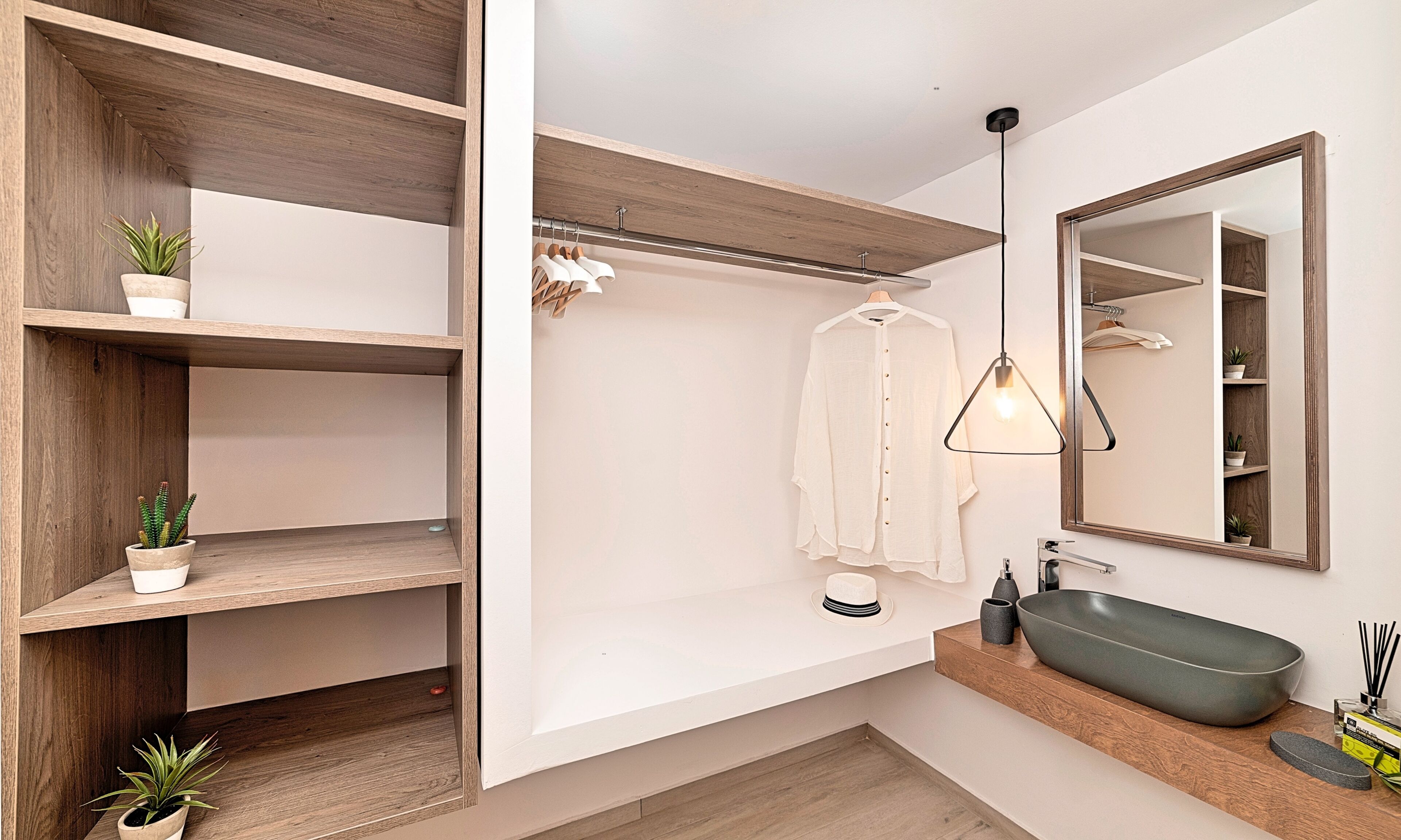 A modern bathroom with a wooden vanity, a large mirror, and built-in shelves with potted plants.