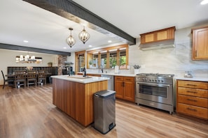 A modern kitchen with wooden cabinetry, a central island, stainless steel appliances, and a dining area with a chandelier. - Vintage 2BR Carlton retreat with hot tub, EV charging, and game room. (Carlton)