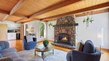Una sala de estar con chimenea de piedra, vigas de madera y plantas colgantes.