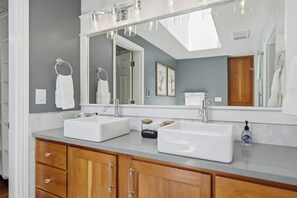A bathroom with two sinks, a large mirror, wooden cabinets, and a skylight. - Vintage Terrace Suite (Newberg)