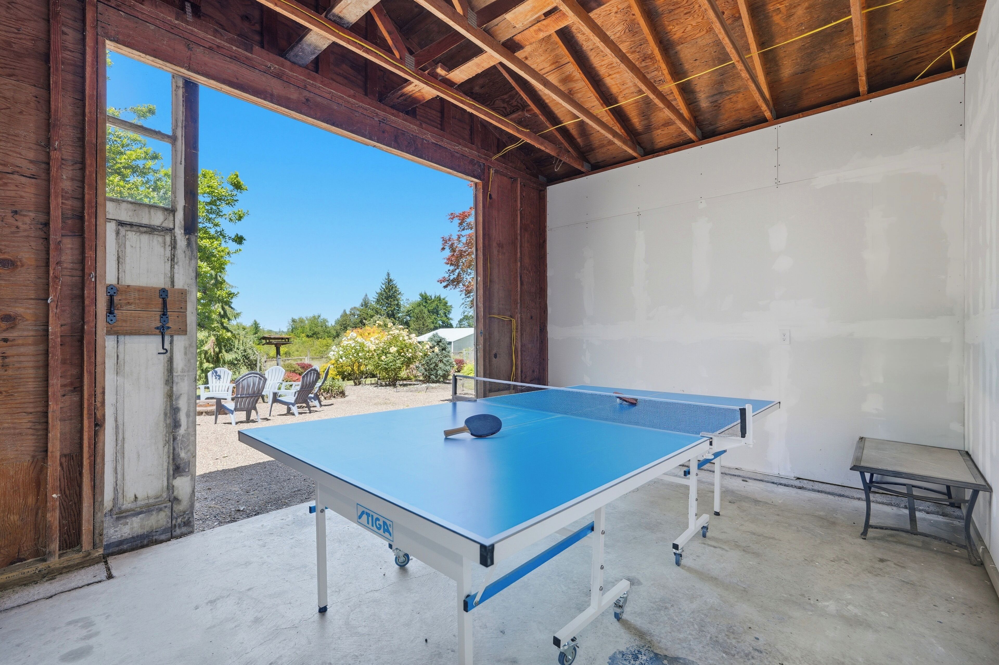 Une table de ping-pong dans une pièce dotée d’un plafond en bois et offrant une vue sur le mobilier d’une terrasse extérieure.