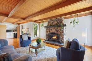 Ein Wohnzimmer mit Kamin aus Stein, Holzbalken und hängenden Pflanzen.