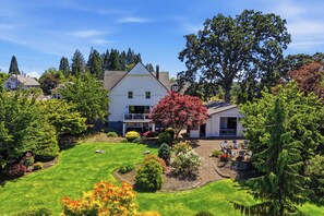 A two-story house with a well-maintained lawn, a patio with outdoor furniture, and a large tree in the front yard. - 5BR Carlton guesthouse with hot tub, patio, and fire pit (Carlton)