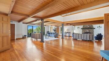 A spacious room with wooden flooring, a stone fireplace, and a large window.