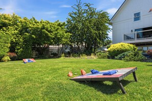 A grassy yard with a wooden deck, trees, and a white building in the background. - 5BR Carlton guesthouse with hot tub, patio, and fire pit (Carlton)