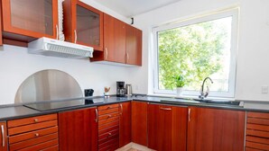 A modern kitchen with wooden cabinets, a stainless steel range hood, a black countertop, and a window with a view of trees. - 10 Person Holiday Home in Bovlingbjerg (Bøvlingbjerg)