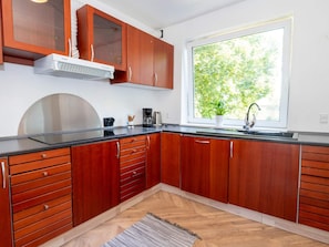 A modern kitchen with wooden cabinets, a stainless steel range hood, a black countertop, and a window with a view of trees. - 10 Person Holiday Home in Bovlingbjerg (Bøvlingbjerg)