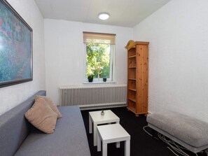 A small, well-lit room with a grey sofa, a white coffee table, a wooden bookshelf, and a radiator under a window. - 10 Person Holiday Home in Bovlingbjerg (Bøvlingbjerg)