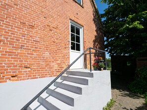 A brick building with a white door and a set of concrete stairs leading up to a porch area with potted plants. - 10 Person Holiday Home in Bovlingbjerg (Bøvlingbjerg)