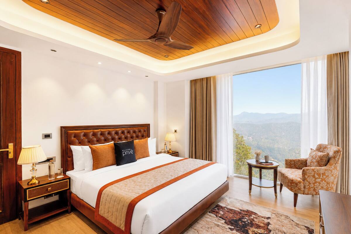 A hotel room with a large bed, a ceiling fan, a nightstand with a lamp, a chair, and a view of the mountains.