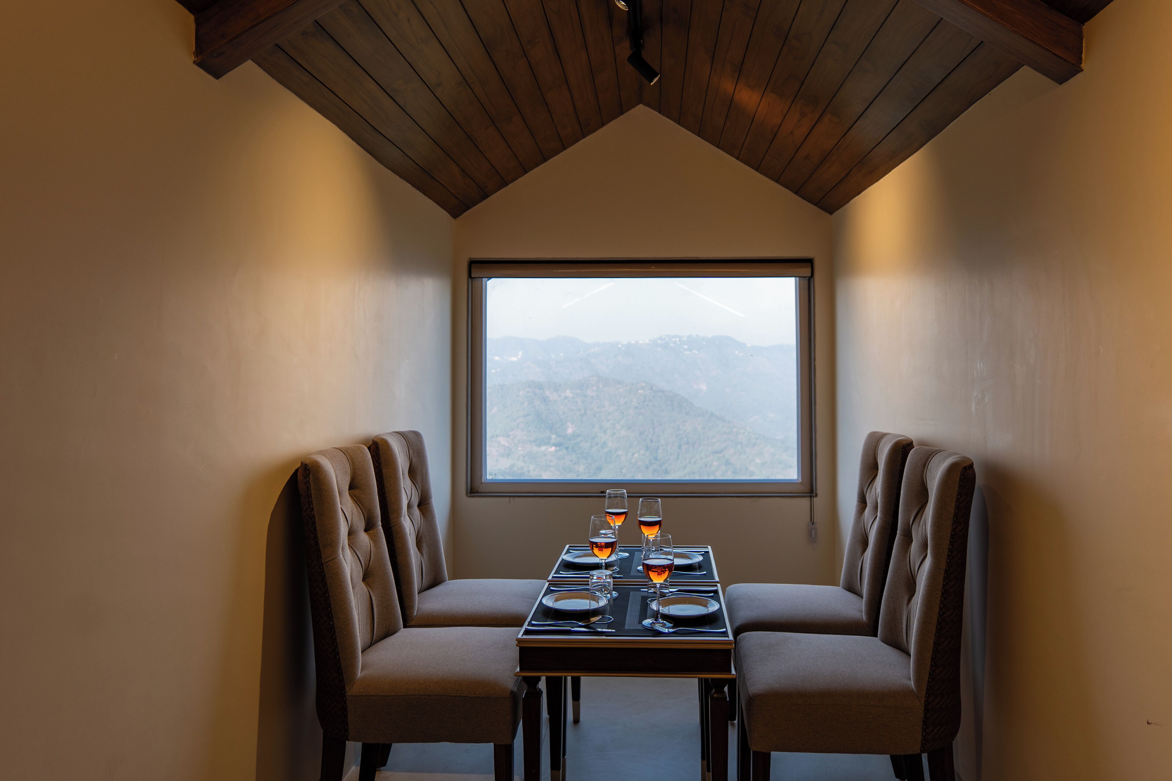 A dining area with two cushioned chairs, a table set for two, and a large window offering a mountain view.