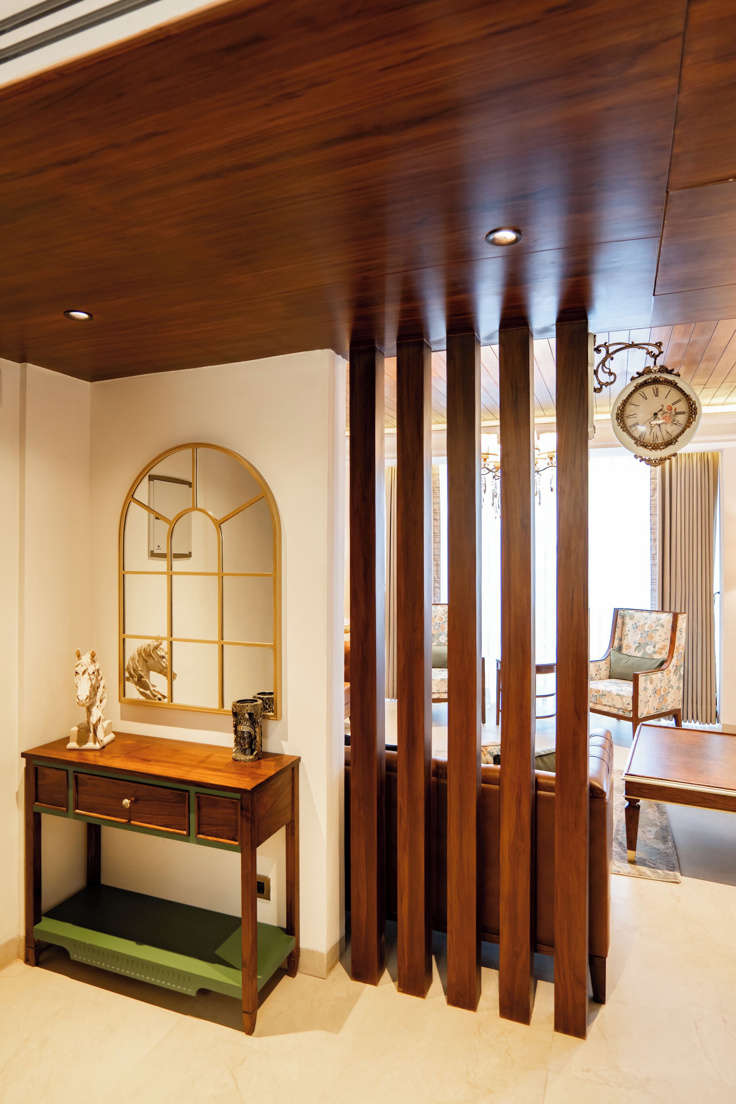 A room with a wooden ceiling, a desk with drawers, a mirror, and a clock.