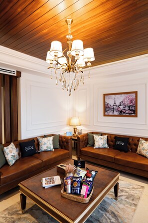 A living room with a brown leather sofa, a coffee table with snacks, a chandelier, and a framed picture on the wall.